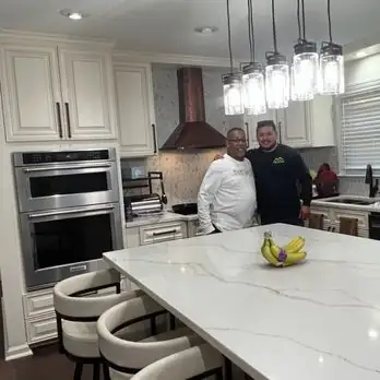 Two men standing in a finished white kitchen with a copper range hood and a white quartz island