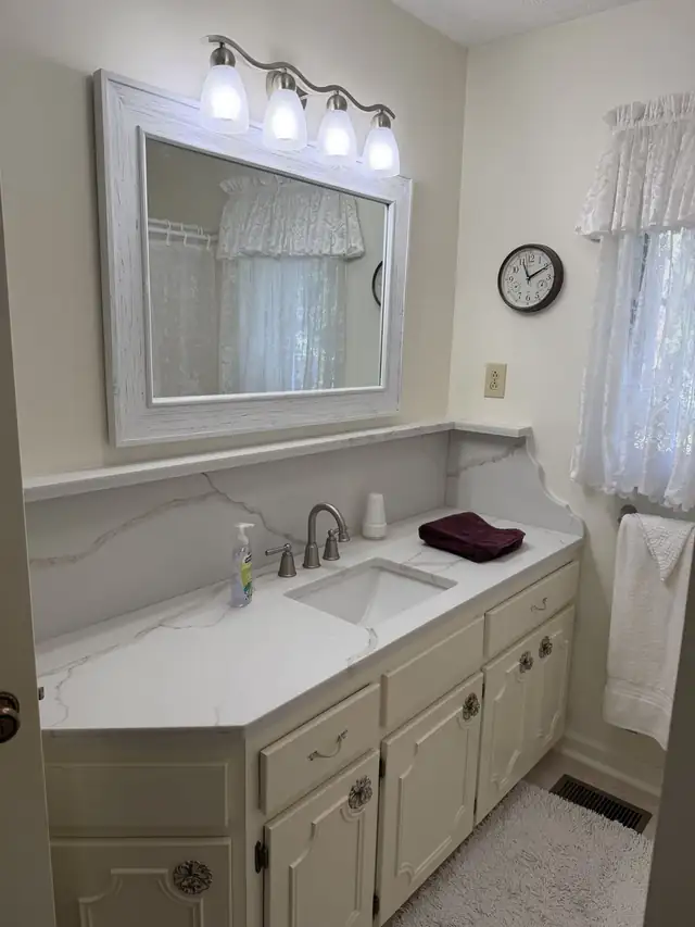 Bathroom vanity with a white veined countertop and backsplash under a framed mirror