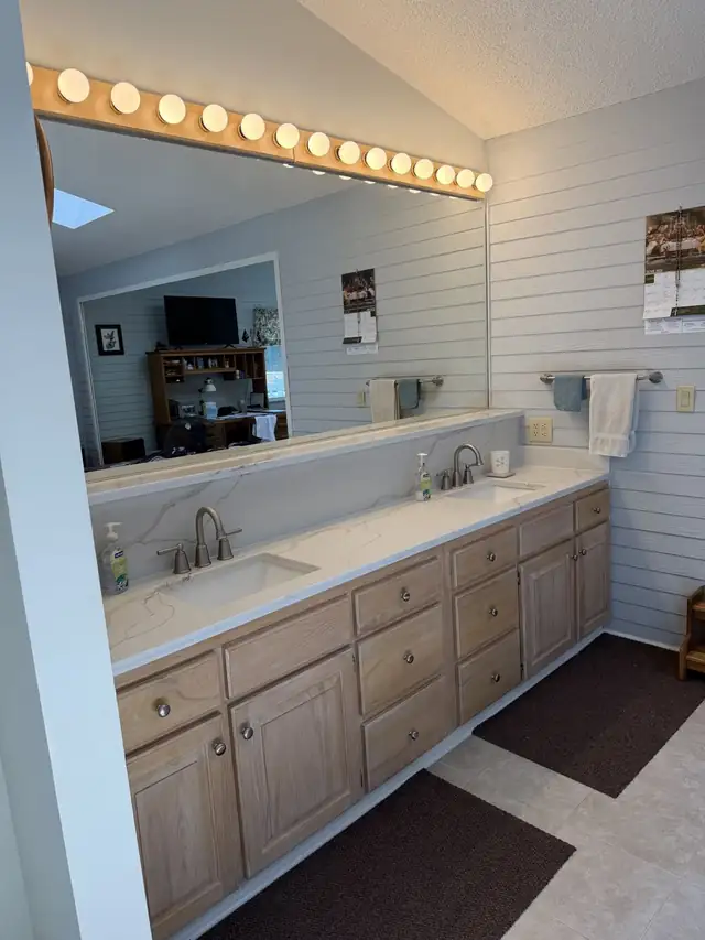 Long bathroom vanity with a white quartz top, two undermount sinks and light wood drawers
